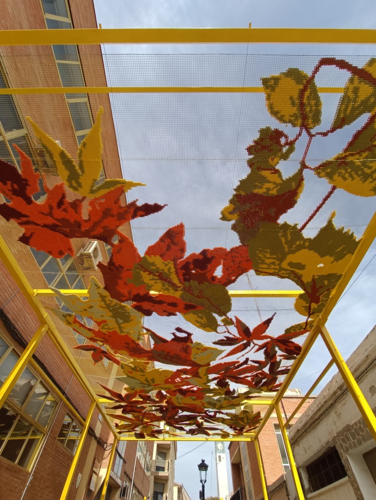 Katarsis — shade structure seen from below, autumn leaves against the sky