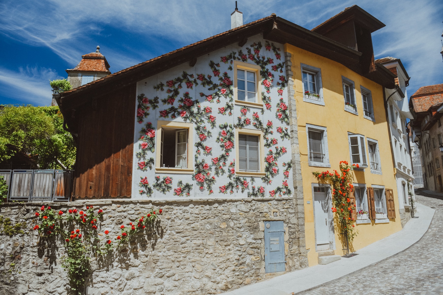 Flores — side view of embroidered facade with real roses on stone wall below